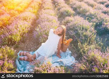 Little adorable girl in lavender flowers field on picnic. Beautiful girl in lavender flowers field at sunset in white dress