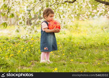 Little adorable girl in the garden, plays with ball