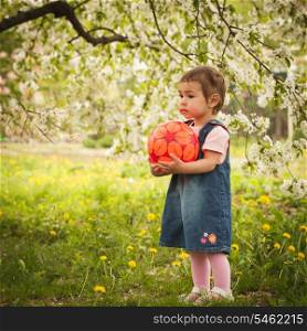 Little adorable girl in the garden, plays with ball