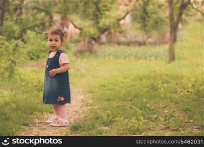 Little adorable girl in the garden, walks on the path