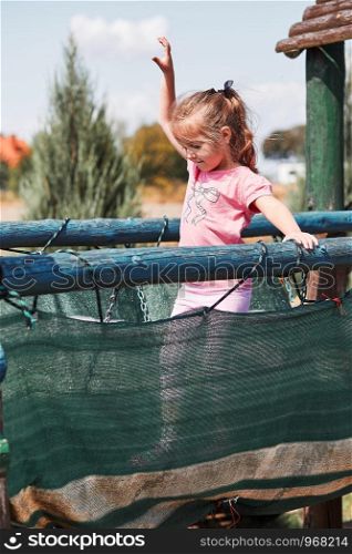 Little adorable girl playing in a home playground in a backyard. Happy smiling kid having fun on a play house on summer day. Real people, authentic situations