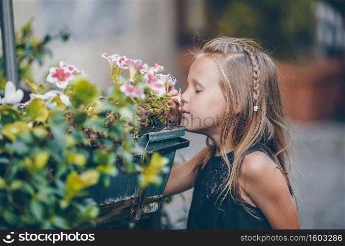 Little adorable girl smelling colorful flowers outdoors in the city. Little adorable girl sitting near colorful flowers in the garden