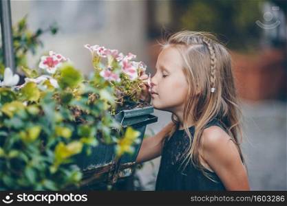 Little adorable girl smelling colorful flowers outdoors in the city. Little adorable girl sitting near colorful flowers in the garden