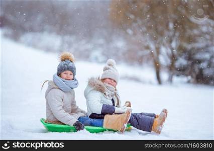 Little adorable girls enjoy a sleigh ride. Kids sledding and playing outdoors in snow. Family vacation on Christmas eve outdoors. Adorable little happy girls sledding in winter snowy day.