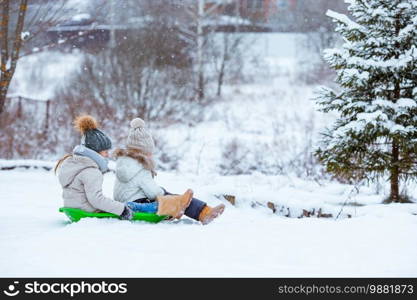 Little adorable girls enjoy a sleigh ride. Kids sledding and playing outdoors in snow. Family vacation on Christmas eve outdoors. Adorable little happy girls sledding in winter snowy day.