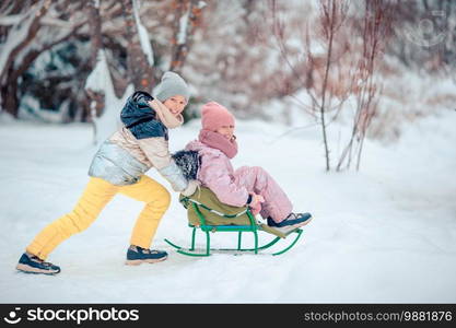 Little adorable girls enjoy a sleigh ride. Kids sledding and playing outdoors in snow. Family vacation on Christmas eve outdoors. Adorable little happy girls sledding in winter snowy day.