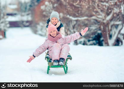 Little adorable girls enjoy a sleigh ride. Kids sledding and playing outdoors in snow. Winter time. Adorable little happy girls sledding in winter snowy day.