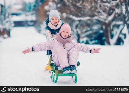 Little adorable girls enjoy a sleigh ride. Kids sledding and playing outdoors in snow. Family vacation on Christmas eve outdoors. Adorable little happy girls sledding in winter snowy day.