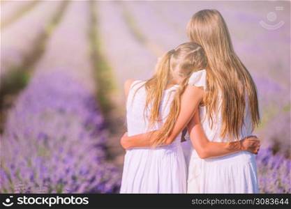 Little adorable girls in lavender flowers field in white dresses enjoy summer vacation. Girls in lavender flowers field at sunset in white dress