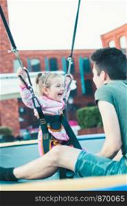 Little adorable smiling girl jumping on trampoline, having fun with her brother at funfair