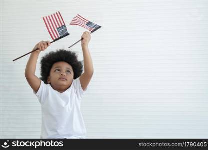 Little African American boy holding waving small USA flags and looking at its at home on white background