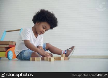 Little African American kid boy sitting on the floor and playing wooden toys at living room at home on white background