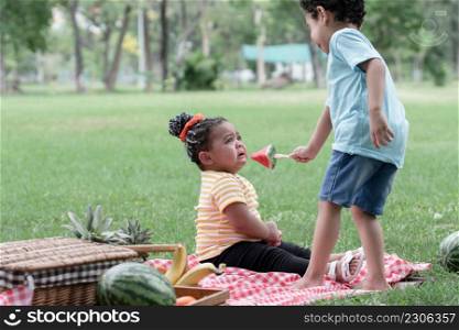 Little African American kids picnic and playing in the park. Little cute girl crying and boy consoling his friend with giving her a piece of watermelon. Friendship of diverse ethnicity children