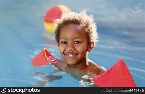 Little african child in the pool . Little african child with orange sleeve floats in the pool