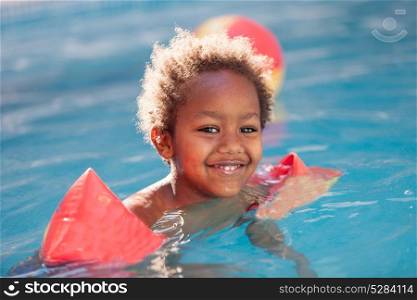 Little african child with orange sleeve floats in the pool