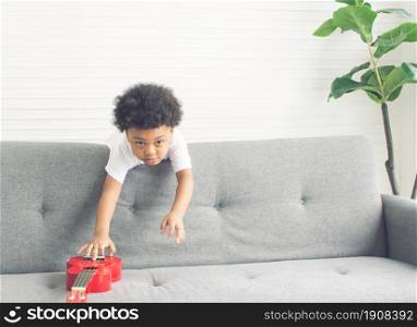 Little african cute and naughty boy playing on sofa in living room at home. Education Concept.