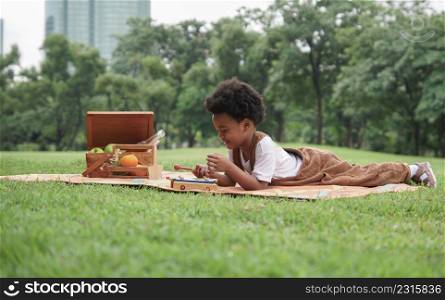 Little African kid boy crying and holding a sore finger when playing xylophone toys alone with sad face at park and lying down on mat with picnic basket on weekend