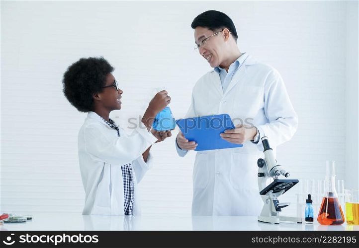 Little African kid boy scientist smiling and showing test bottle filled with chemistry liquid to Asian teacher man while he doing chemical science experiment in laboratory at school