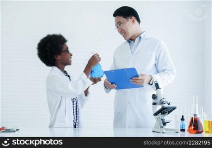 Little African kid boy scientist smiling and showing test bottle filled with chemistry liquid to Asian teacher man while he doing chemical science experiment in laboratory at school