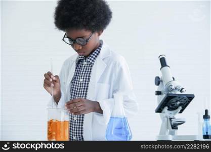 Little African kid boy scientist wear glasses concentrated with stirring chemistry liquid in test bottle while he doing chemical science experiment in laboratory at school