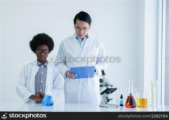 Little African kid boy studying chemistry and doing chemical science experiment in laboratory at school with Asian teacher man