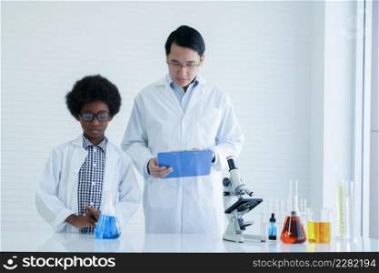 Little African kid boy studying chemistry and doing chemical science experiment in laboratory at school with Asian teacher man