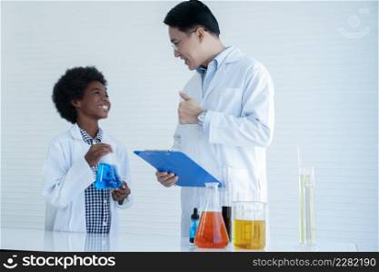 Little African kid boy studying chemistry and doing chemical science experiment in laboratory at school. Happy dark skinned boy showing test bottle to Asian teacher man and he thumbs up with smile