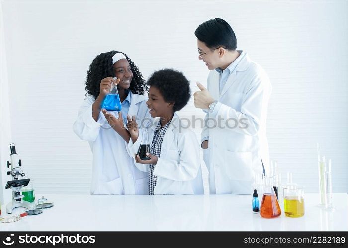 Little African kids studying chemistry and doing chemical science experiment in laboratory at school. Happy dark skinned girl showing test bottle to Asian teacher man and he thumbs up