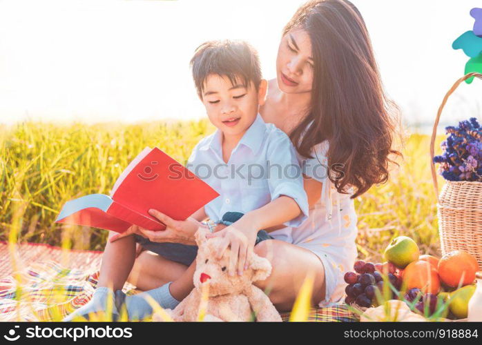 Little Asian boy and his mother reading books when doing picnic in meadow. Mother and son learning together. Celebrating in Mother day and appreciating concept. Summer people and lifestyle education