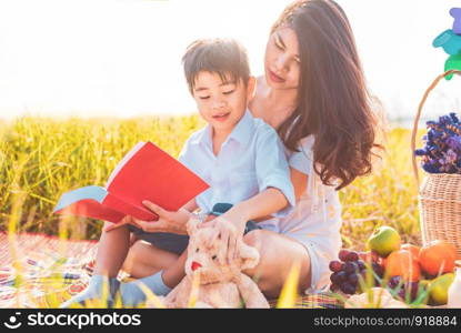 Little Asian boy and his mother reading books when doing picnic in meadow. Mother and son learning together. Celebrating in Mother day and appreciating concept. Summer people and lifestyle education