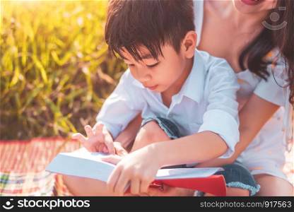 Little Asian boy and his mother reading tale story books at meadow field. Mother and son learning together. Celebrating in Mother day and appreciating concept. Summer people and lifestyle education