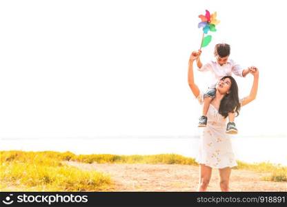 Little Asian boy riding back on his super power mom in meadow near lake. Mother and son playing together. Celebrating in Mother day and appreciating concept. Summer people and lifestyle theme.