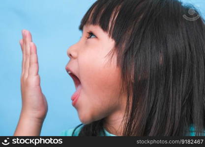 Little asian girl covering her mouth to smell the bad breath. Child girl checking breath with her hands. Oral health problems or dental care concept.