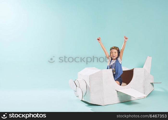 Little asian girl is happy sitting on a hand made cardboard paper plane . Isolated on mint green background .