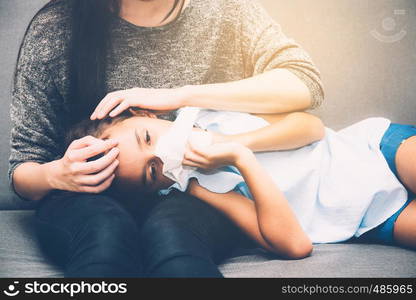 Little asian girl is sick weak lying on sofa with mother of take care and touching forehead in living room - family health concept.