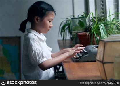 Little asian girl using old vintage typewriter to studying