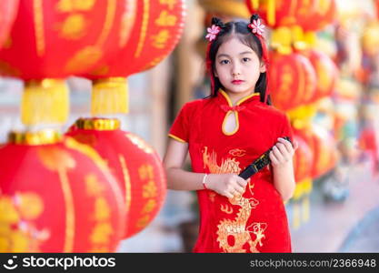 little Asian girl wearing red traditional Chinese cheongsam and holding a Fanningand lanterns with the Chinese alphabet Blessings written on it Is a Fortune blessing compliment decoration for New Year