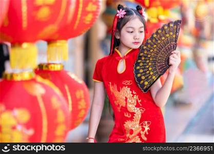 little Asian girl wearing red traditional Chinese cheongsam and holding a Fanningand lanterns with the Chinese alphabet Blessings written on it Is a Fortune blessing compliment decoration for New Year