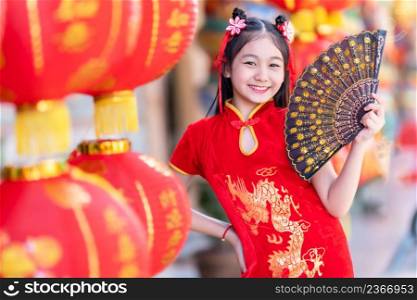 little Asian girl wearing red traditional Chinese cheongsam and holding a Fanningand lanterns with the Chinese alphabet Blessings written on it Is a Fortune blessing compliment decoration for New Year