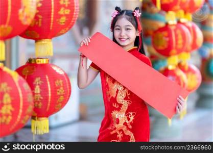 little Asian girl wearing red traditional Chinese cheongsam decoration show blank paper red and lanterns with the Chinese text Blessings written on it Is a Fortune blessing for Chinese New Year