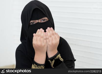 Little Asian Pakistani Muslim girl wearing black hijab with beautiful eyes is praying to god. White background