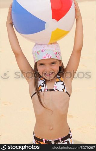 Little at the beach holding inflatable ball above head