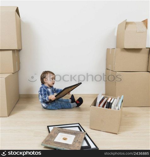 little baby boy sitting moving cardboard boxes looking picture frame new home
