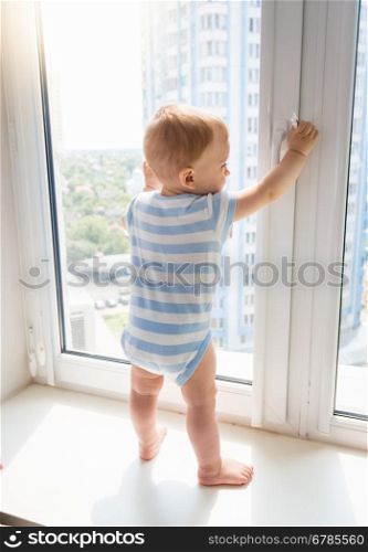 Little baby boy standing on window sill and pulling window handle, Concept of children in danger
