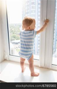 Little baby boy standing on window sill and pulling window handle, Concept of children in danger