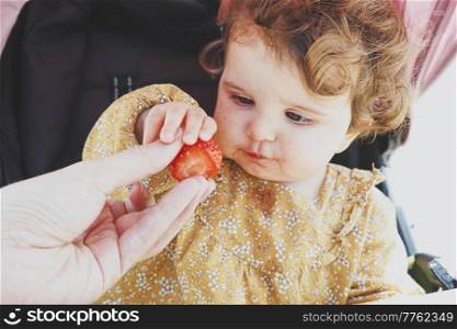 Little baby girl eating a strawberry