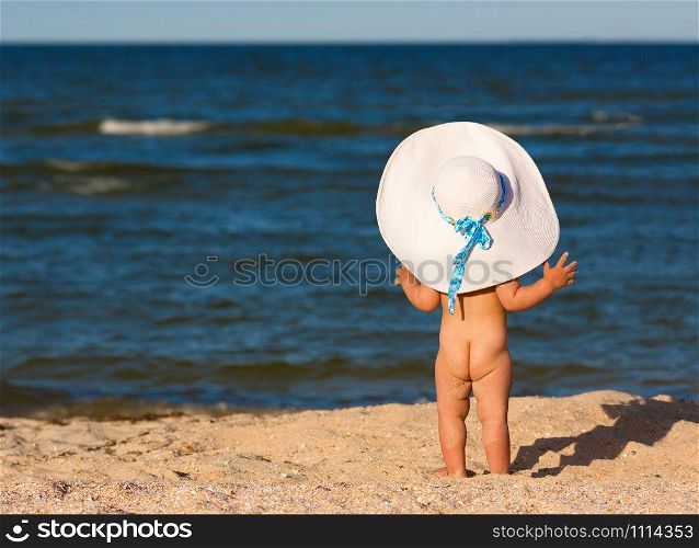Little baby girl in big hat on the beach looking at sea