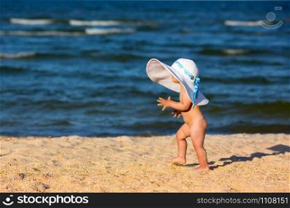 Little baby girl in big hat walking on the beach