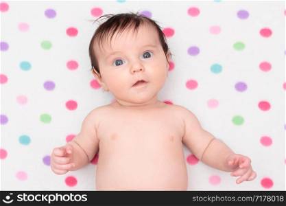 Little baby girl lying on blanket with colourful polka dots
