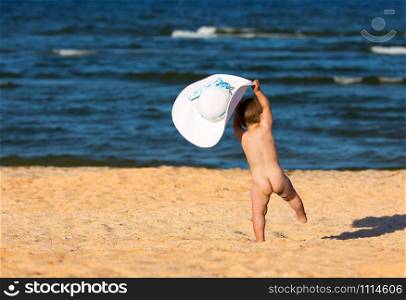Little baby girl with big hat in the wind on the beach